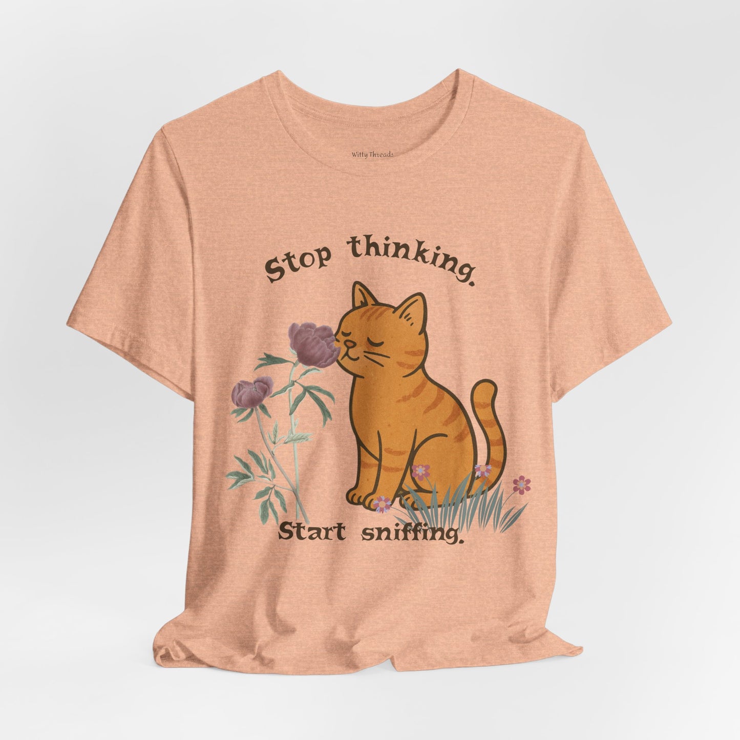 Peach t-shirt with a cat sniffing flower graphic and text 'Stop thinking. Start sniffing.' in brown.