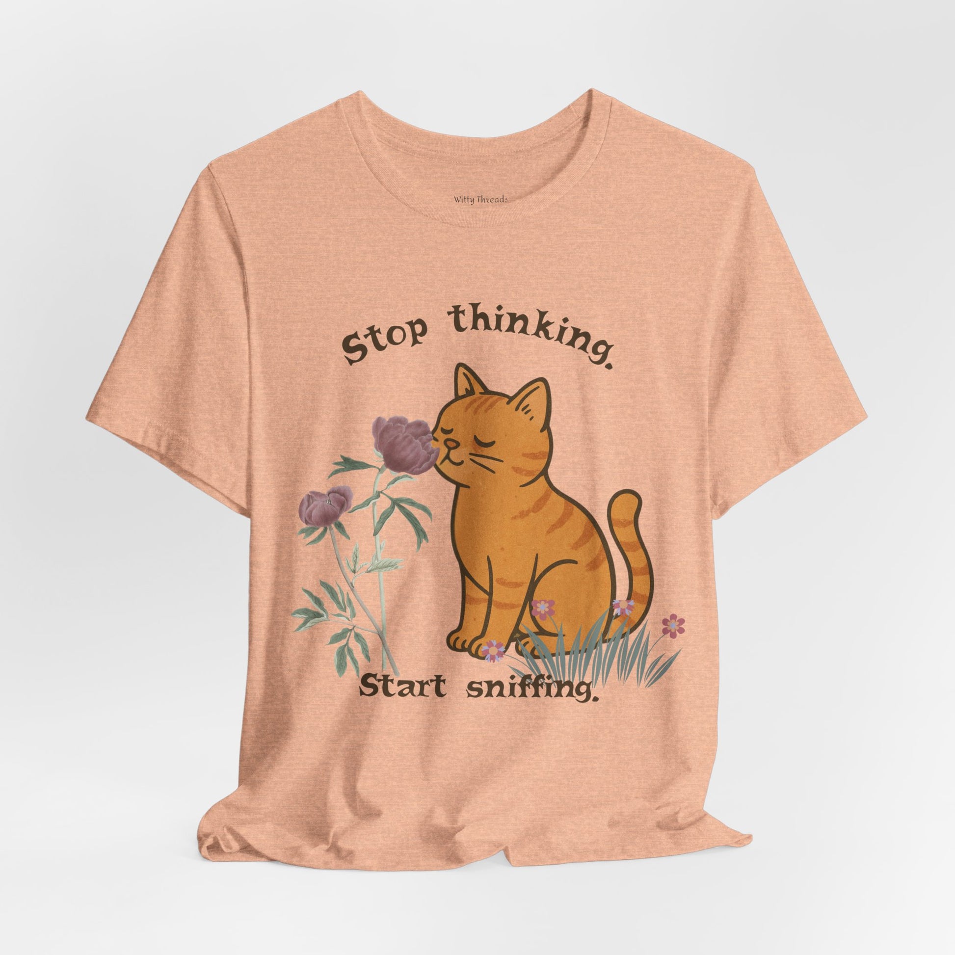 Peach t-shirt with a cat sniffing flower graphic and text 'Stop thinking. Start sniffing.' in brown.
